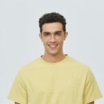 Réalisations Portrait of a young man wearing glasses and a yellow shirt, smiling brightly.