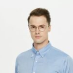 Réalisations Professional portrait of a man wearing glasses and a blue shirt, isolated on white background.